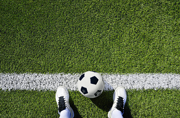 Secondary Football Boots: an image showing a downward view of someone's feet with football boots on, and a football placed between both feet, while standing on the sideline